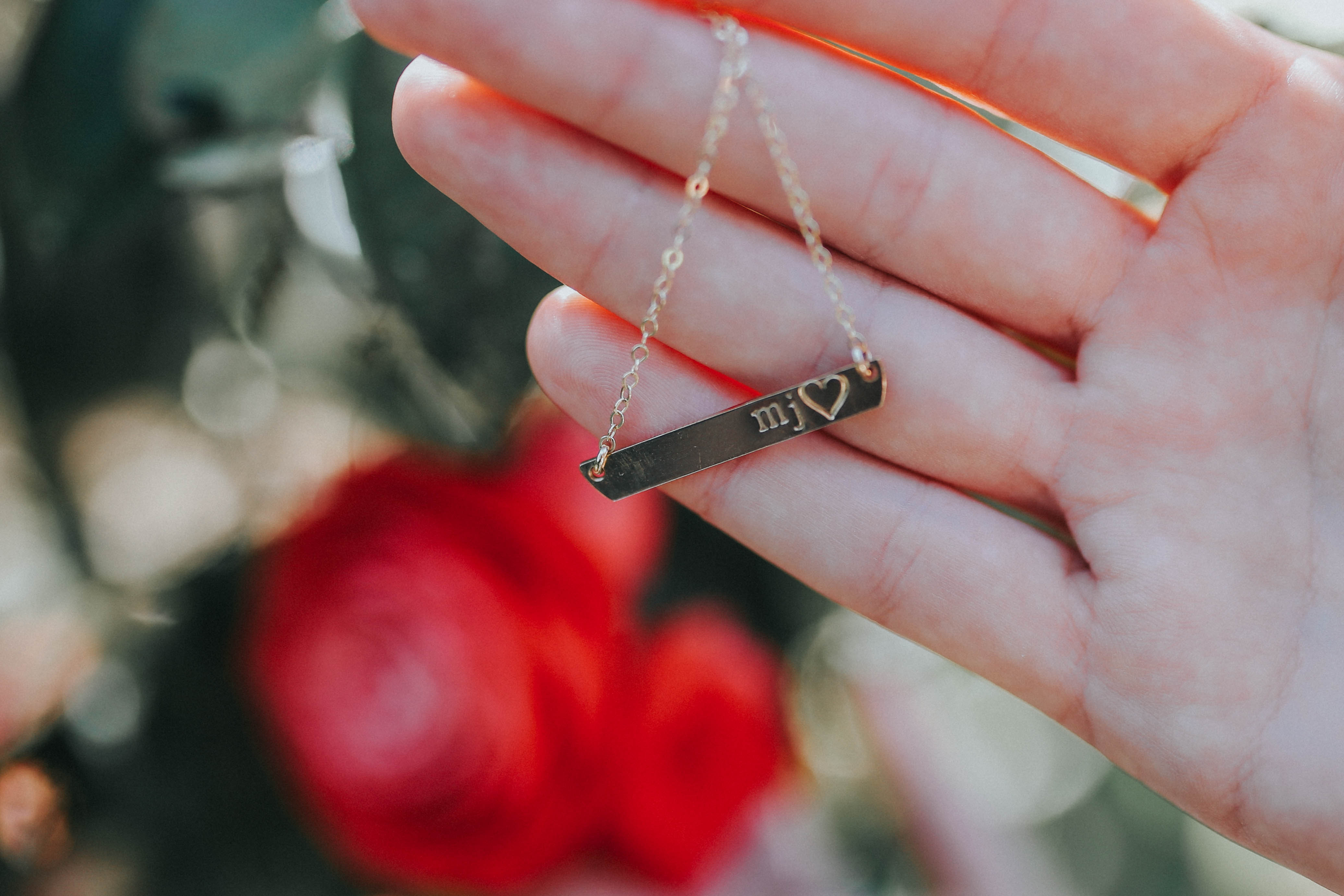 Model holds the 14K Gold Filled Personalized Name Plate Necklace with roses in the background
