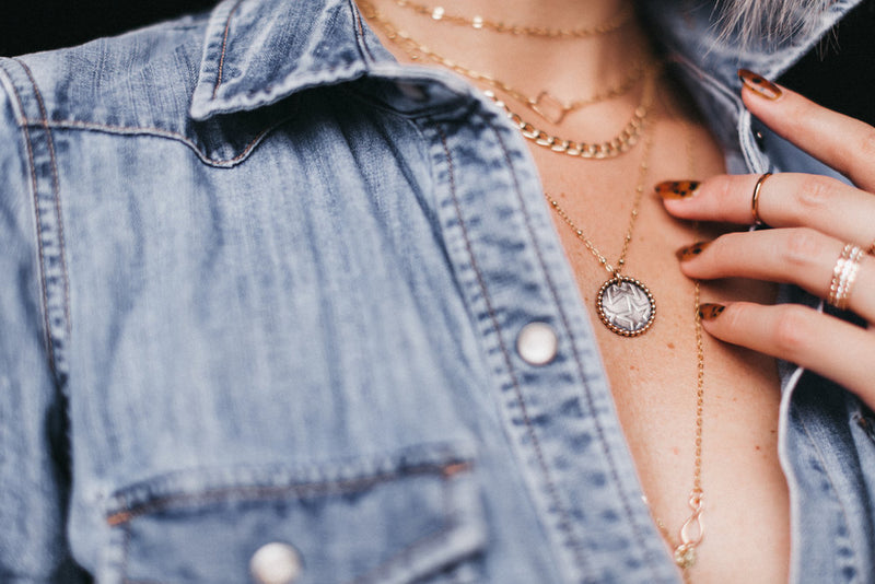 Model styles the Two Tone Coin Pendant Necklace with layering necklaces and a denim shirt
