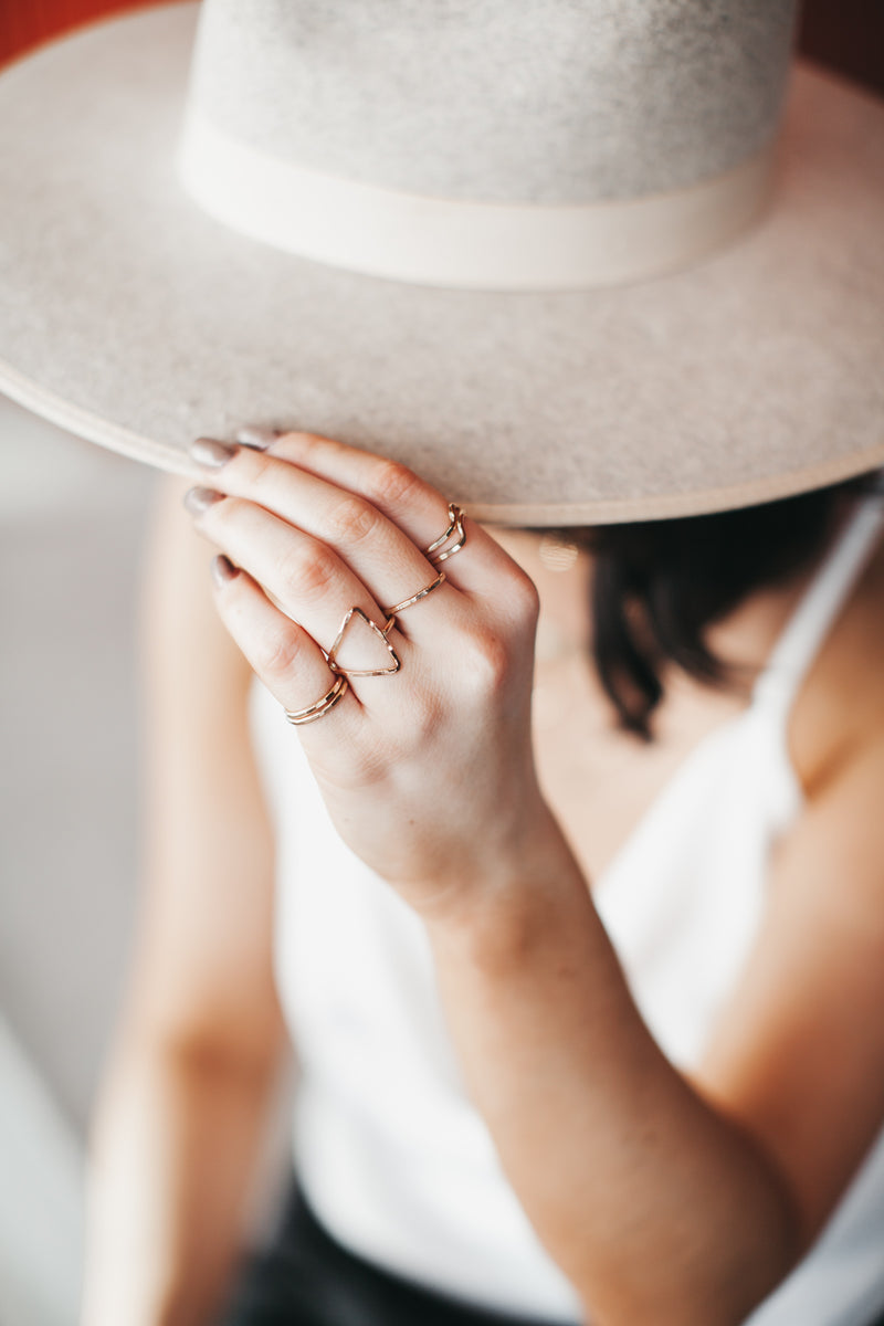 Model wears the Kenda Kist Triangle Ring with stackable band rings and stackable wave rings
